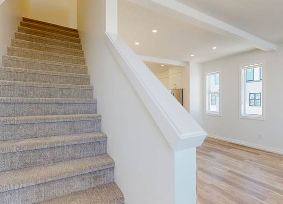 A staircase with a carpeted runner and wooden steps leads up to a bright room with white walls and a window.