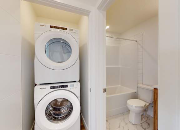 A white washing machine and dryer stacked on top of each other in a small laundry room.