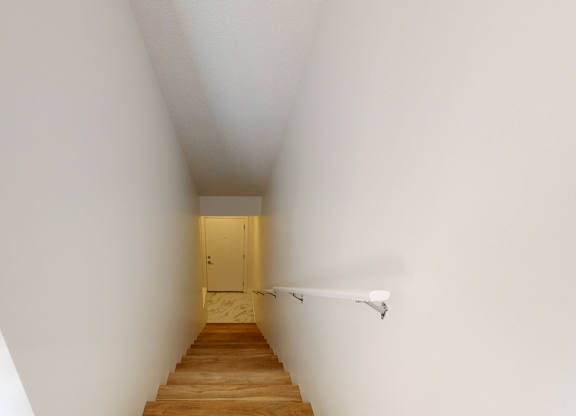 A long hallway with a wooden staircase leading to a door at the end.