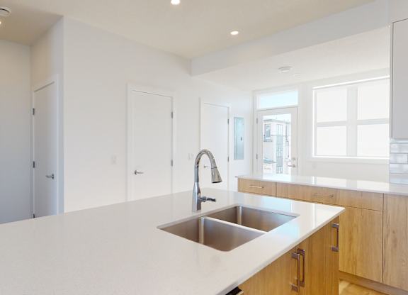 A modern kitchen with a white countertop and a stainless steel sink.
