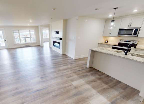 A spacious kitchen and living room with wooden flooring and white walls.