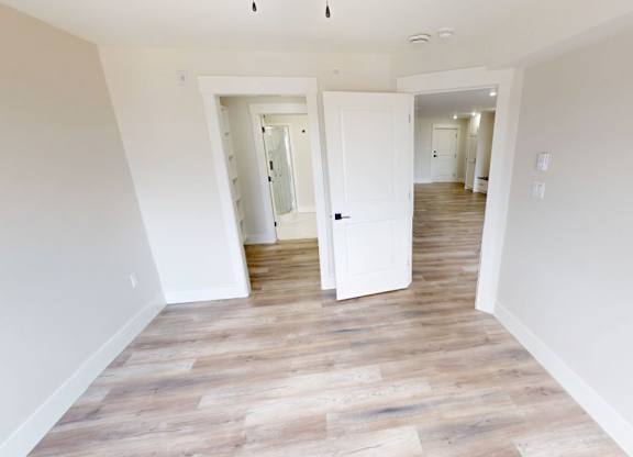 A room with white walls and wooden flooring with two open doors.