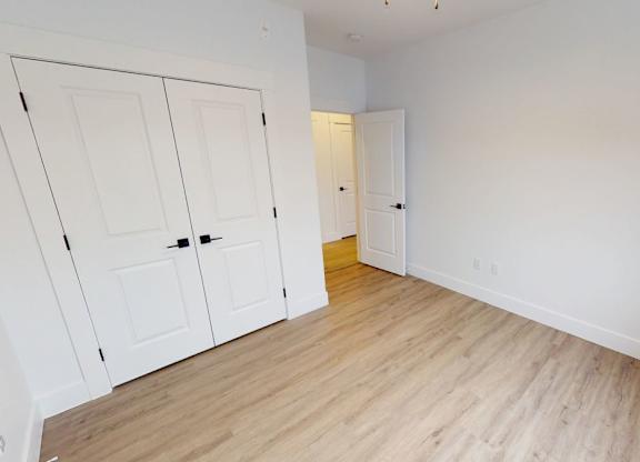 A room with white walls and wooden flooring with two doors.
