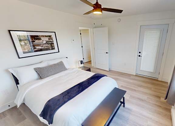 A bedroom with a bed, a ceiling fan, and a picture on the wall.