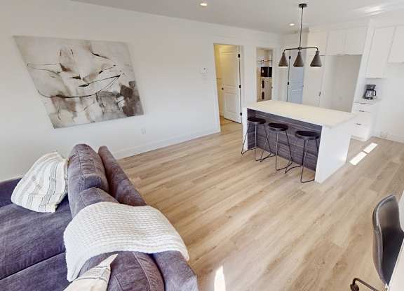A modern living room with a grey couch and a white kitchen in the background.