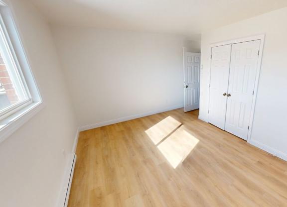 A room with wooden floors and white walls with a door on the right.