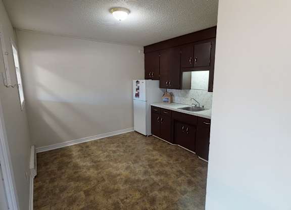 A kitchen area with a refrigerator, sink, and cabinets.