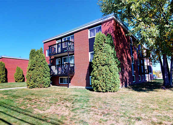 A red brick building with a balcony and trees in front.
