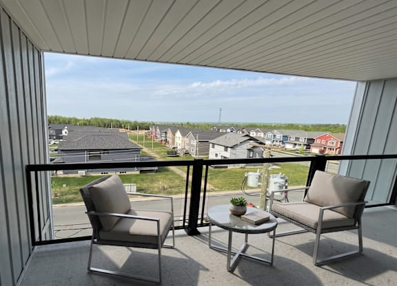 A balcony with two chairs and a table overlooking a residential area.