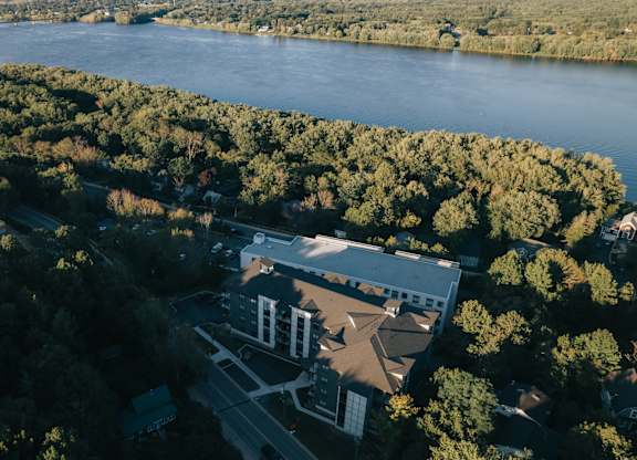 An aerial view of a building surrounded by trees with a body of water in the background.