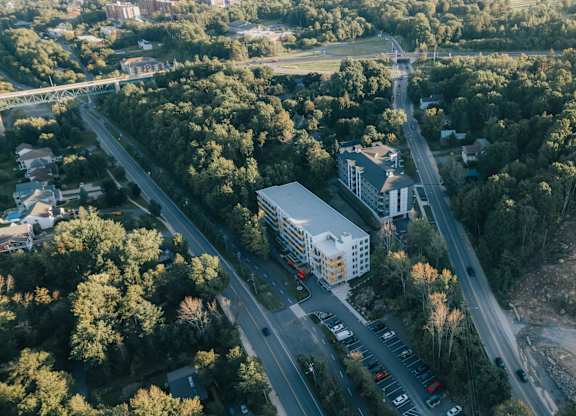 A road with cars and a white building in the middle of a forest.