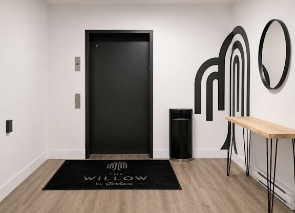 A black door is in a room with a wooden bench and a black trash can.