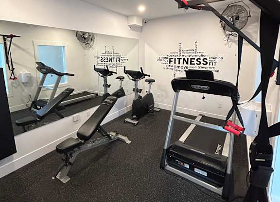 A gym with a variety of equipment including a treadmill, a stationary bike, and a rowing machine.