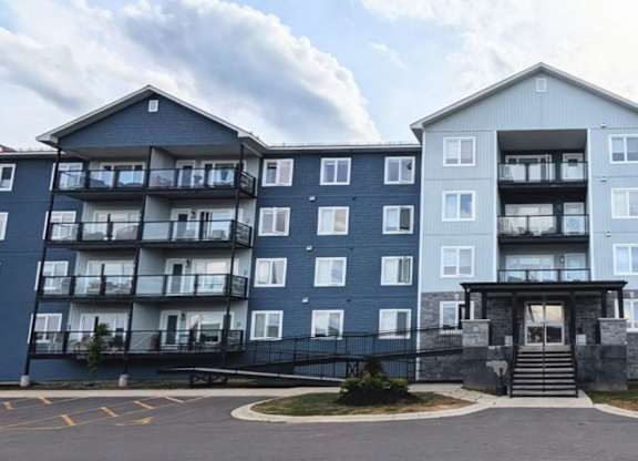 A large blue and white apartment building with a parking lot in front.