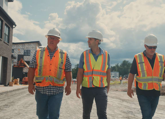 Three construction workers wearing safety vests and hard hats walking on a construction site.