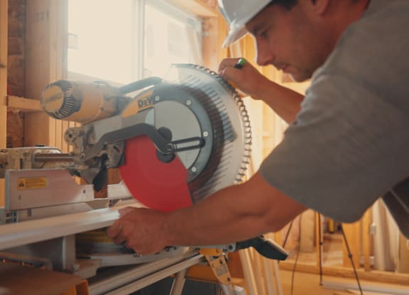 A man in a hard hat is using a circular saw to cut a piece of wood.
