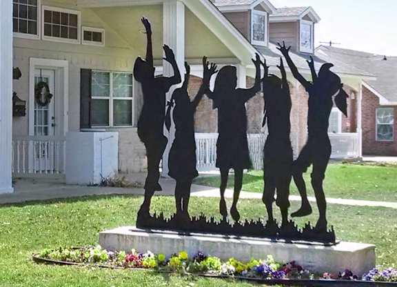 A statue of four people dancing is in the foreground of a residential area.
