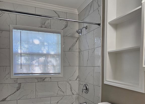 A white toilet sits in a bathroom with a marble tile wall and a window.