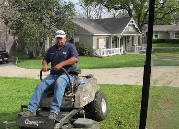 A man in a blue shirt and jeans is riding a Quest lawn mower.