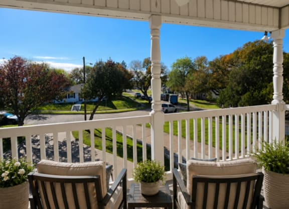 Two chairs and a table on a porch with a view of the street.