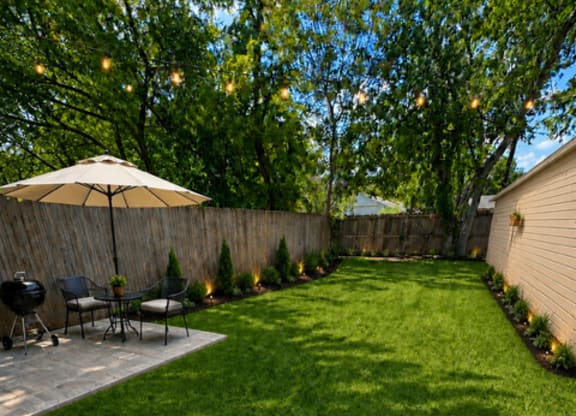 A backyard with a lawn, a patio with chairs and an umbrella, and a fence.