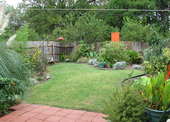A backyard with a green lawn and a brick walkway.