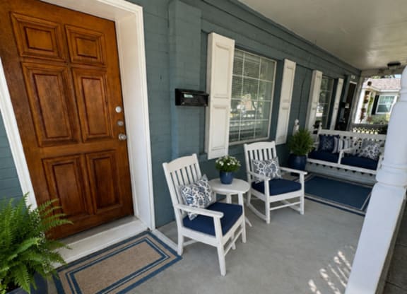 A porch with a wooden door and white chairs.