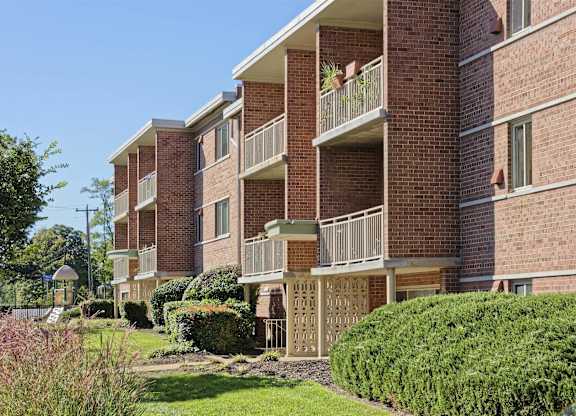 A red brick apartment building with green bushes in front.