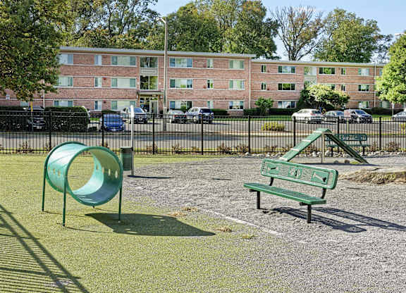A dog park with a green slide and bench in front of a brick building.