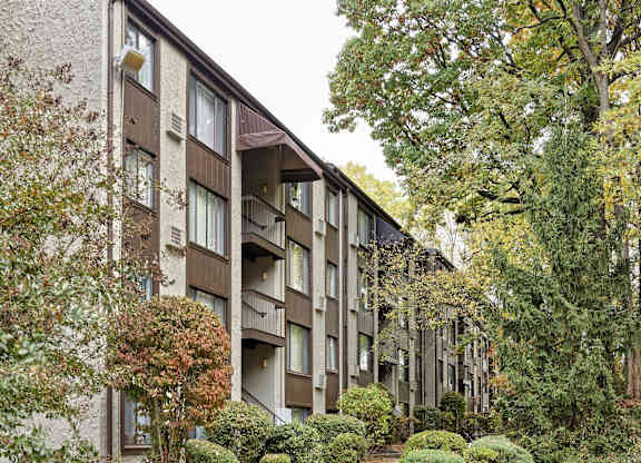 A building with a brown and beige exterior is surrounded by trees and bushes.
