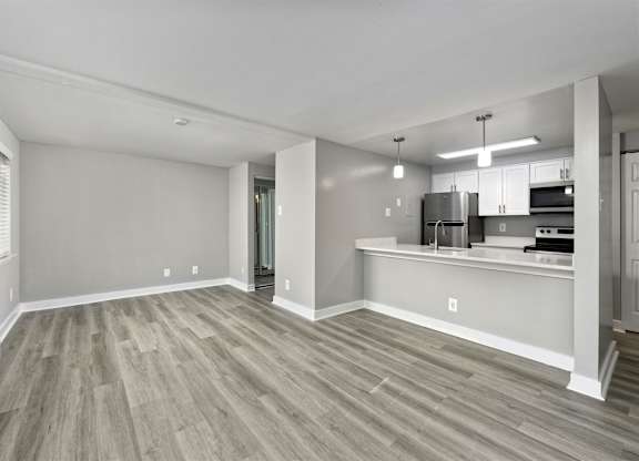 A spacious living room with a wood floor and a kitchen area in the background.
