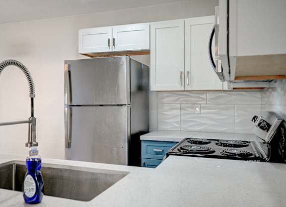 A kitchen with a stainless steel refrigerator, a sink with a blue bottle on it, and a stove with a white pot on it.