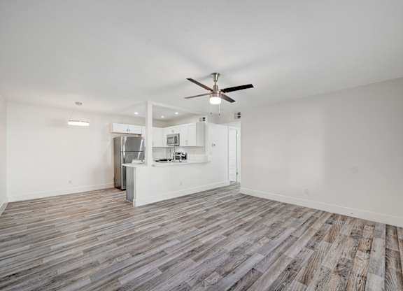 A room with a ceiling fan and a kitchenette in the background.