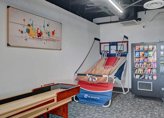 A room with a pool table, a basketball hoop, and a vending machine.