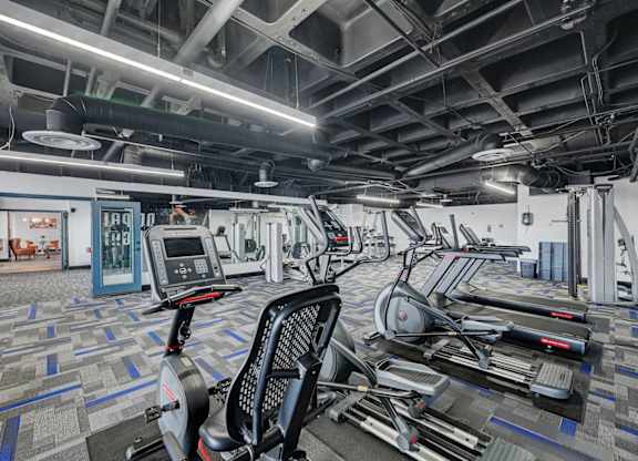 A gym with a variety of exercise equipment including treadmills, stationary bikes, and elliptical machines.