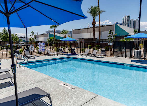 A pool with sun loungers and a blue umbrella.