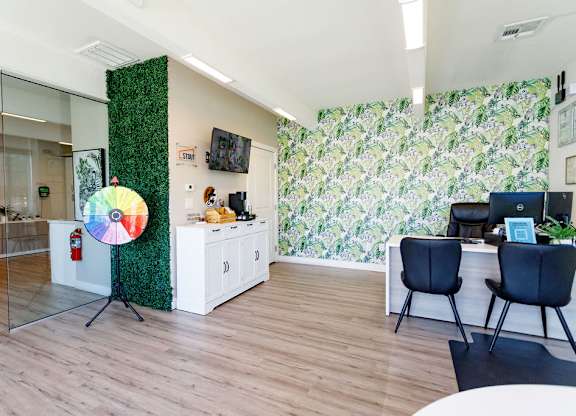 A room with a green plant wallpaper and a white desk with a laptop on it.