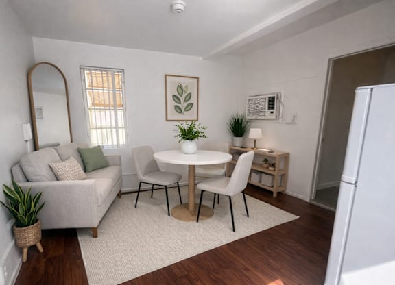 A white dining table with four chairs is in the middle of a room with a couch and a mirror.