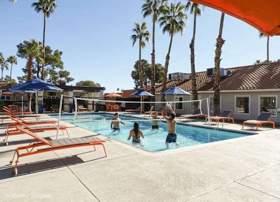 People are swimming in a pool surrounded by palm trees.