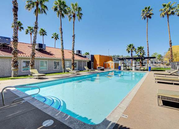 A pool surrounded by palm trees and a building in the background.