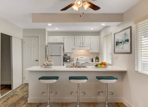 A kitchen with white cabinets and a white island with green bar stools.