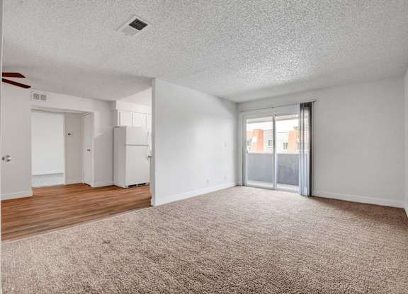 A spacious room with a carpeted floor and a sliding glass door leading to a balcony.