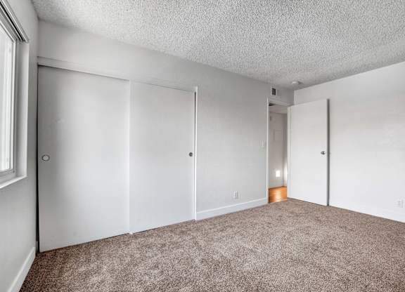 A room with carpeted floor and white walls with a door on the left.