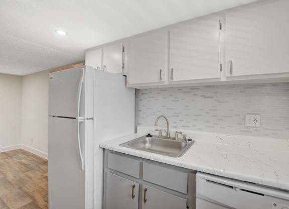 A kitchen with a white refrigerator, marble countertops, and wooden flooring.