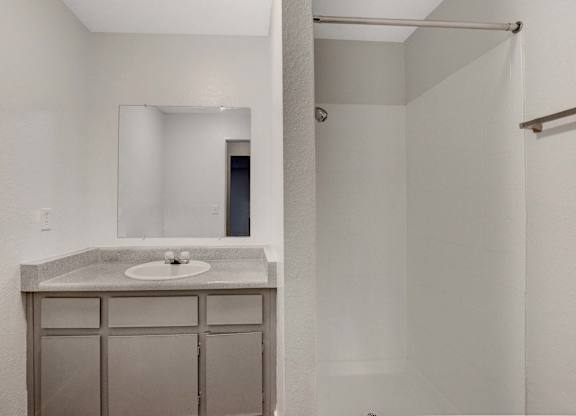 A bathroom with a sink, mirror, and shower.