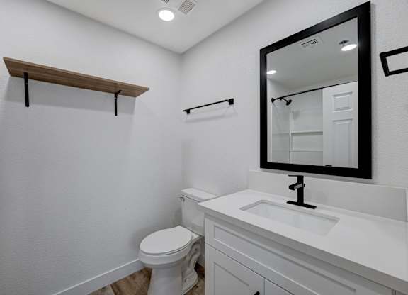 A white bathroom with a toilet, sink, and mirror.