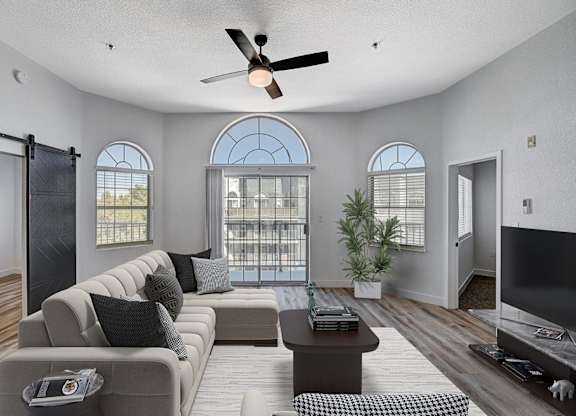 A living room with a grey sofa, a coffee table, a ceiling fan, and a sliding glass door.