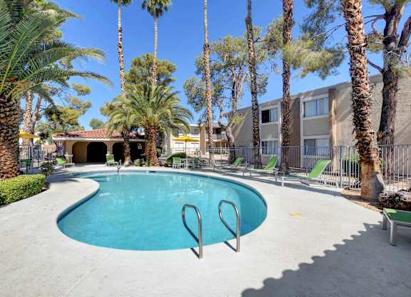 A pool surrounded by palm trees and a building in the background.