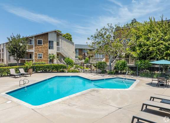 A swimming pool surrounded by lounge chairs and trees in a residential area.