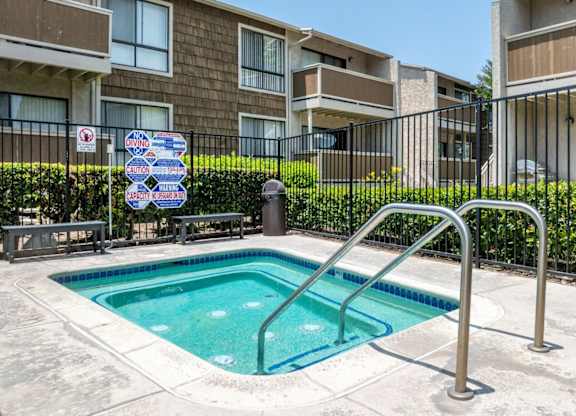 A small pool surrounded by a metal fence with a sign on it.